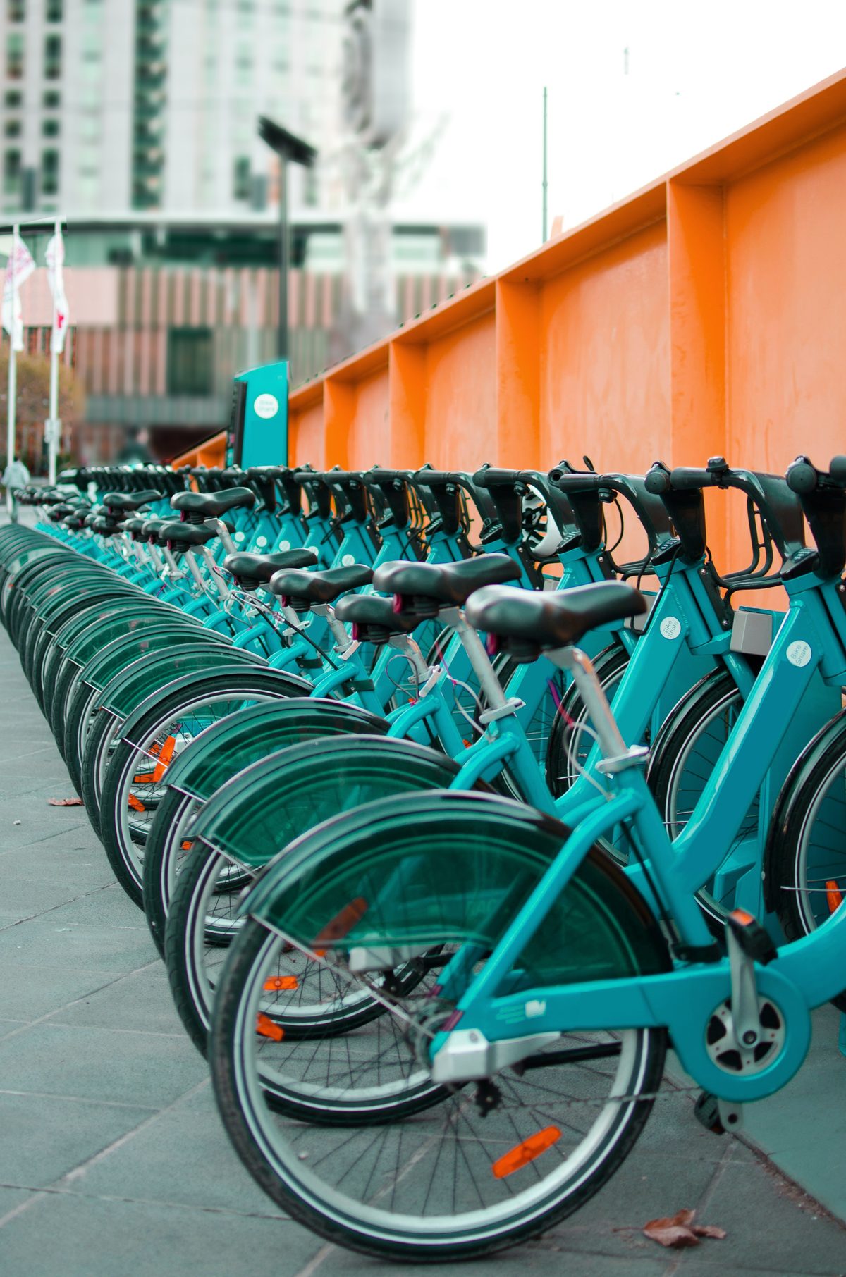 Row of teal city bikes parked along an orange wall