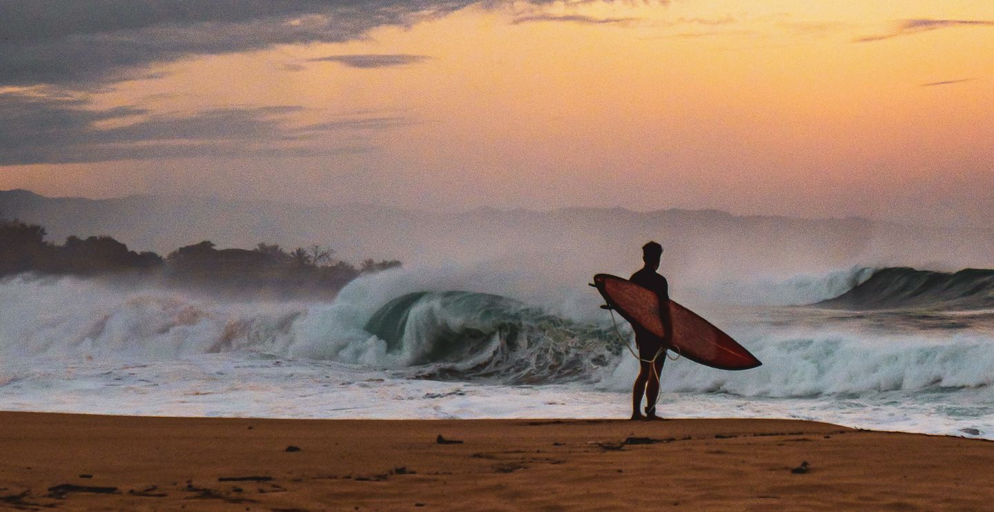 Surfer facing the ocean at dawn, board under the arm