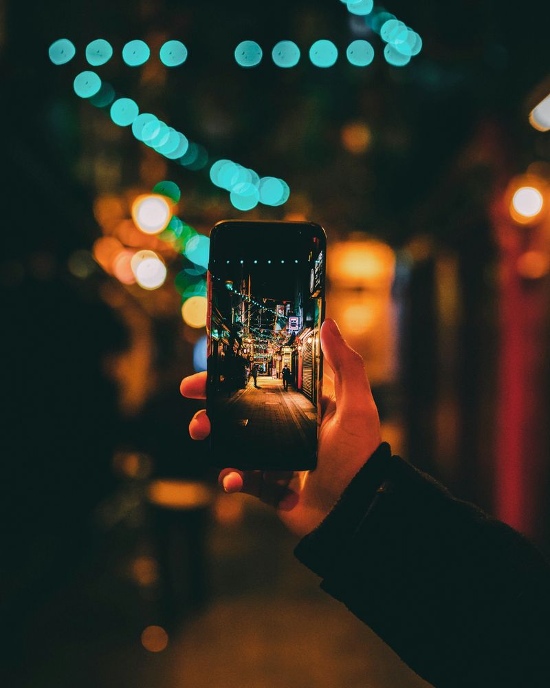 Hand holding a phone filming a street at night, lights out of focus